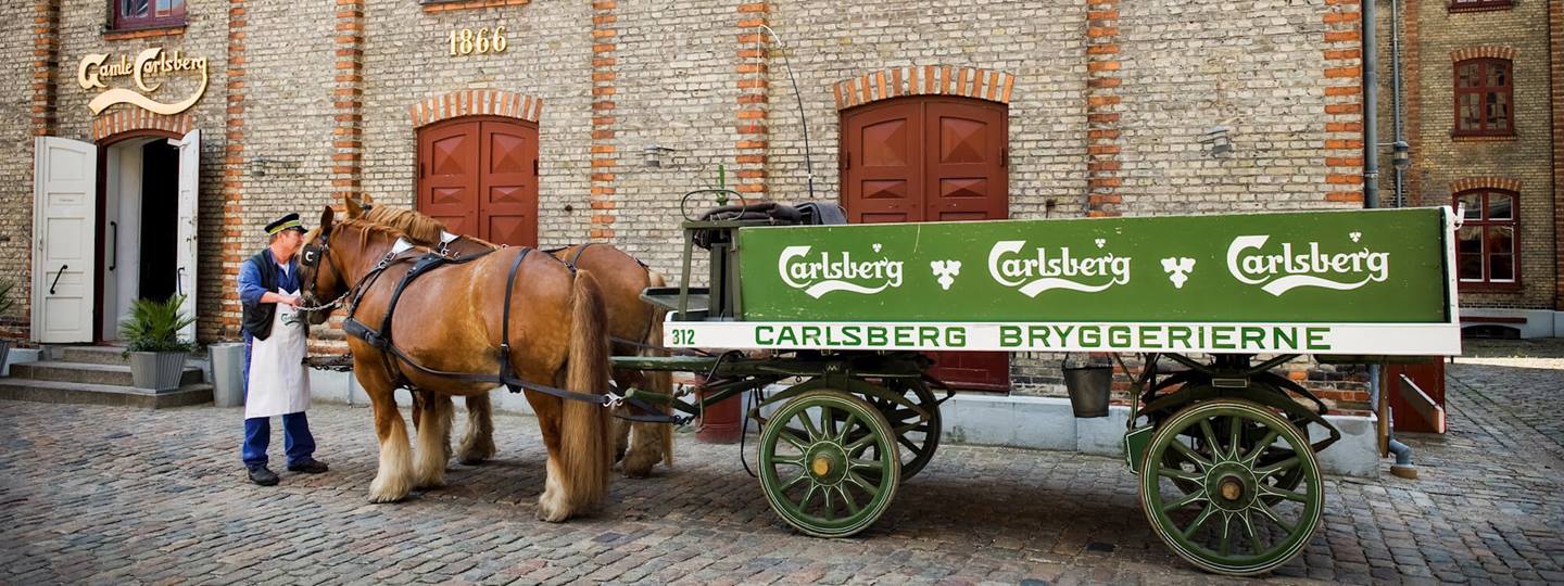 2 horses in with a wagon in front of a brick budling