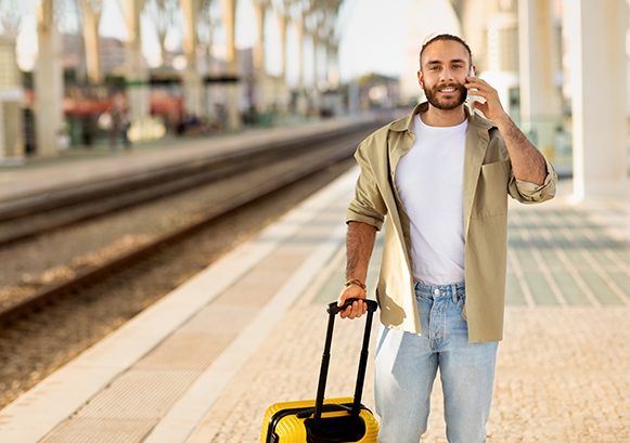 A man at a train station with a suitcase talking on a phone