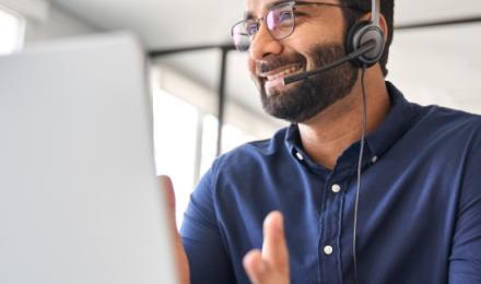 Man talking with his headset on and facing his laptop