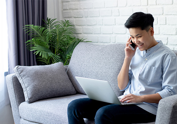 Man on the phone on the sofa smiling and looking at his laptop