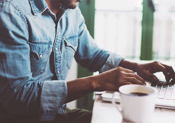 A guy working on a computer with a coffee on his side