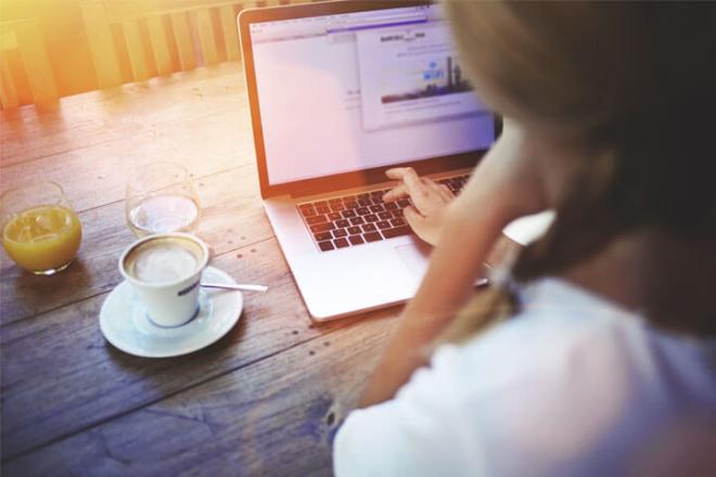 A woman in front of her laptop with a coffee on the side