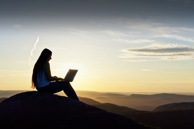 A woman looking at her laptop during the sunset 